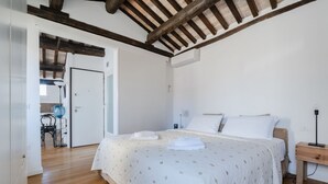 Een slaapkamer met een houten plafond, een bed met witte beddengoed, een nachtkastje en een stoel op de achtergrond.