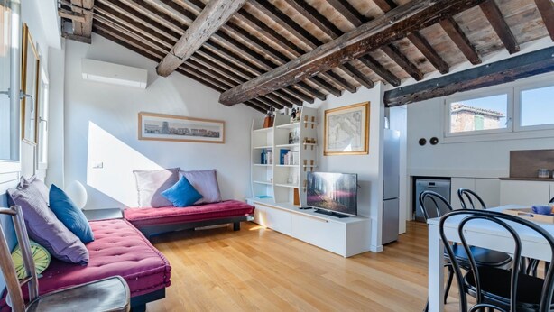 Een moderne woonkamer met een houten plafond, een rode bank, een televisie en een eethoek met stoelen.