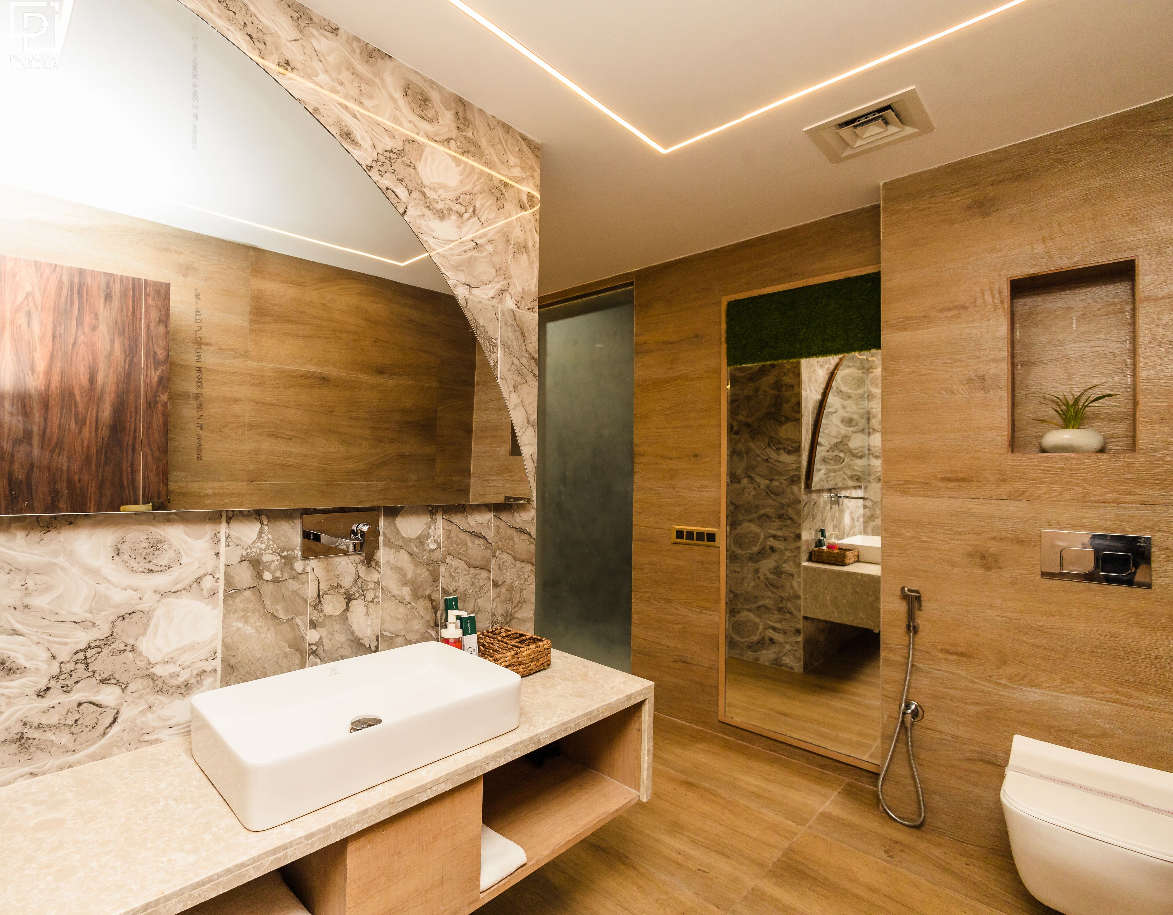 Un baño moderno con tocador de mármol, muebles de madera, ducha integrada y una pequeña planta en la pared.