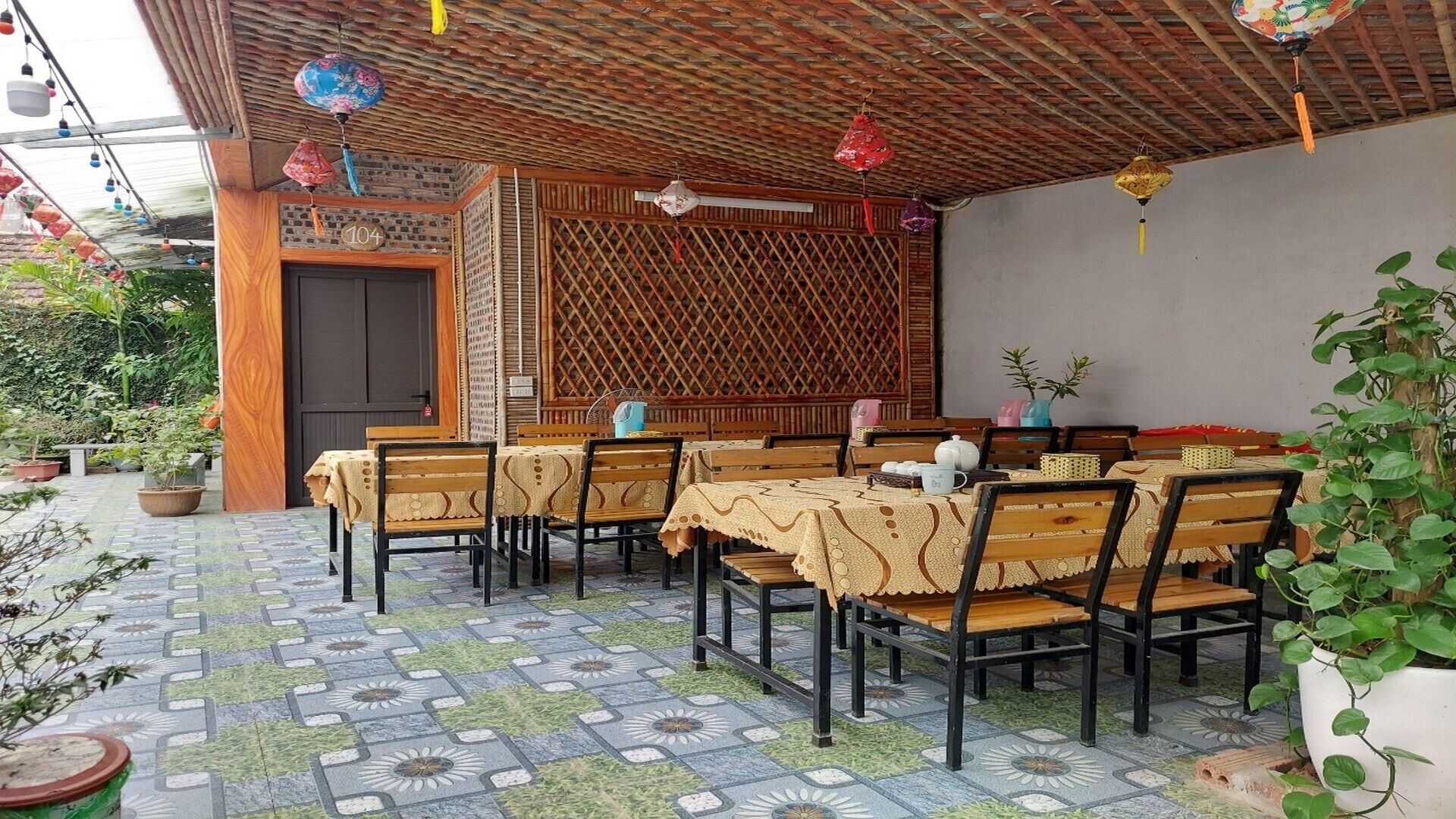 Un área de comedor al aire libre con mesas y sillas de madera, piso estampado y un muro de celosía de madera.