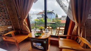 A balcony with wooden furniture, a table with a water bottle and a vase of flowers, and a view of buildings and a water tank in the background. - Tam Coc Koi Homestay (Nam Hoa Lu)