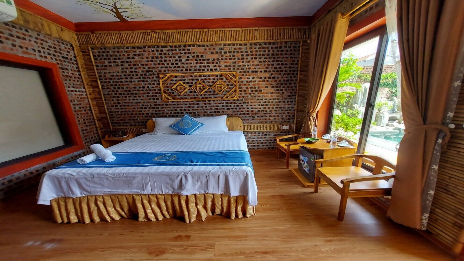A hotel room with a brick-patterned wall, a bed with a blue and white bedspread, a wooden desk, and a chair.