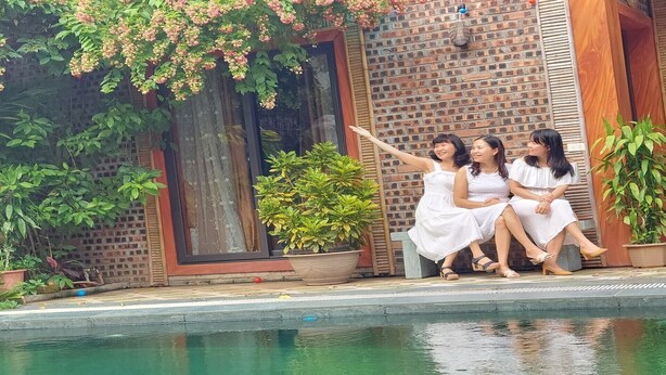 Three women sitting by a poolside with a brick wall and greenery in the background. - Tam Coc Koi Homestay (Nam Hoa Lu)