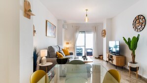 Un salon moderne avec une table basse en verre, des fauteuils jaunes, un canapé gris et un téléviseur posé sur un meuble en bois.