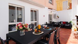 Un espace de restauration en plein air avec une table dressée pour le petit-déjeuner, entourée de chaises, et un canapé en arrière-plan.