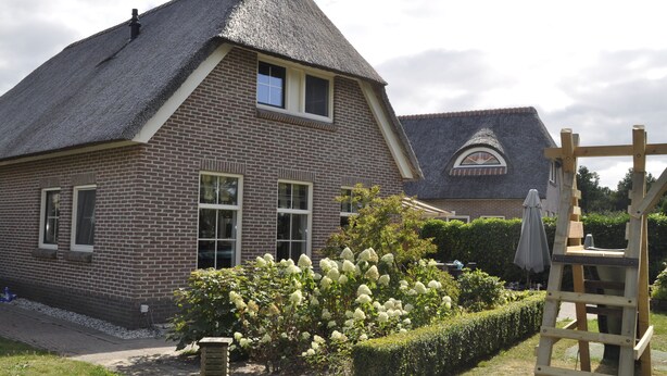 A brick house with a thatched roof, a small window, and a garden with white flowers. - Villa Martensplek with sauna, 10 pers + 2 toddlers (Tiendeveen)