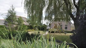 A residential garden with a pond, a wooden swing set, and a brick house with a sloped roof. - Villa Martensplek with sauna, 10 pers + 2 toddlers (Tiendeveen)