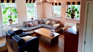 A cozy living room with a sectional sofa, a coffee table, and a dining table. There are potted plants on the windowsills and a sign on the wall. - Villa Martensplek with sauna, 10 pers + 2 toddlers (Tiendeveen)