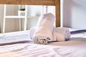 A neatly made bed with rolled white towels and a purple blanket.