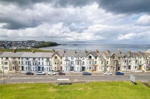 Stunning coastal homes with pitched roofs and bay windows line the quiet street, offering a serene view of the sea.