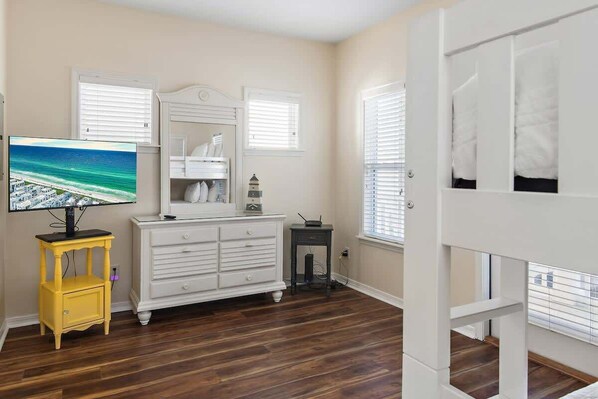 A room with a bunk bed, a dresser, a television, and a window with blinds.