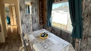 Un coin repas avec une table dressée pour deux personnes, une fenêtre avec des rideaux et une vue sur l’extérieur.