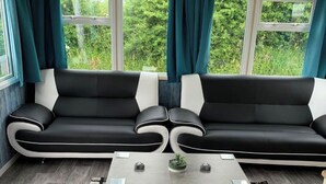 Un salon moderne avec un ensemble de canapés noir et blanc, une table basse et une vue sur la verdure grâce à de grandes fenêtres.