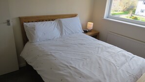 Una cama bien hecha con ropa blanca y un cabecero de madera en una habitación con ventana.