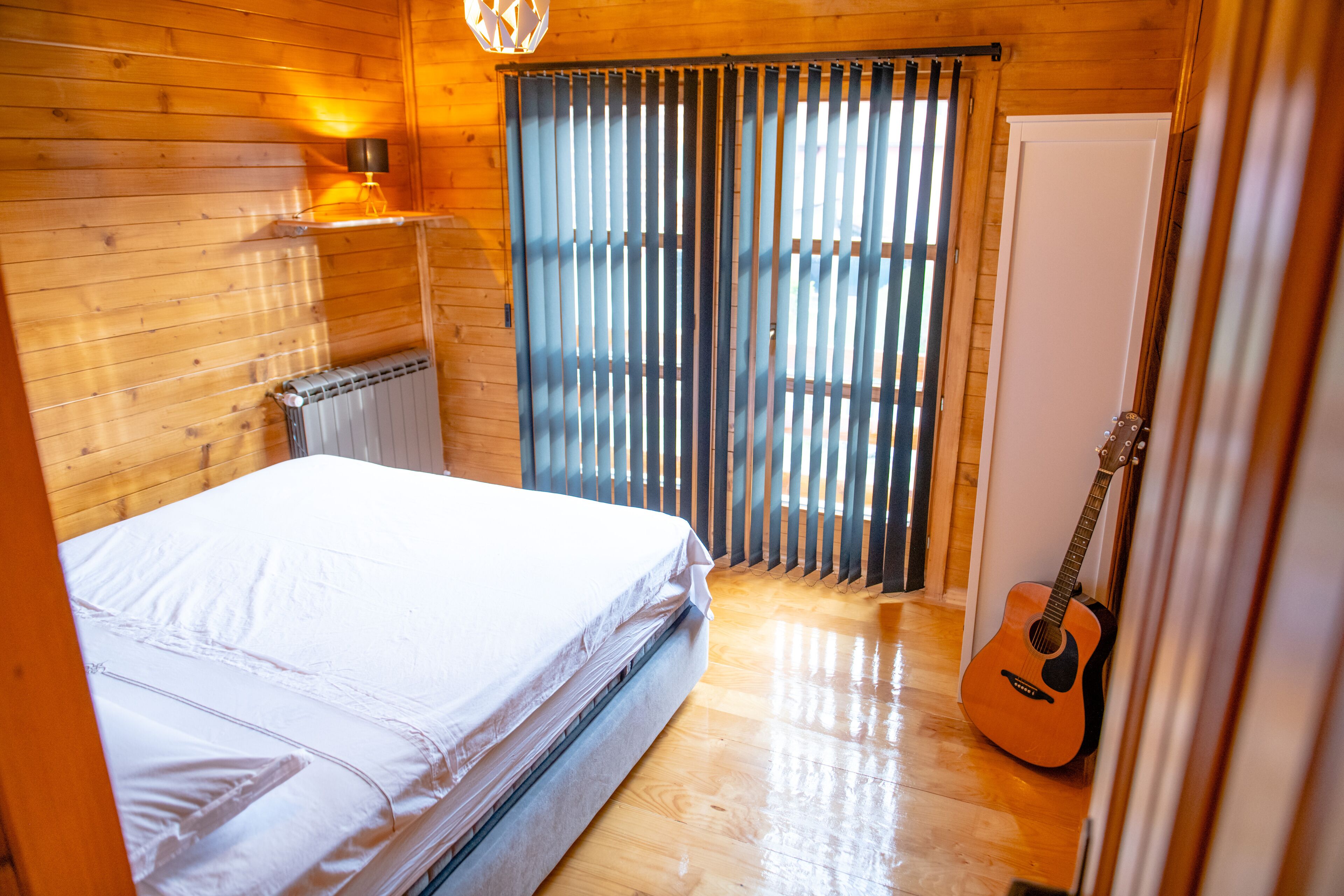 Une pièce en bois avec un lit, une guitare et un radiateur.