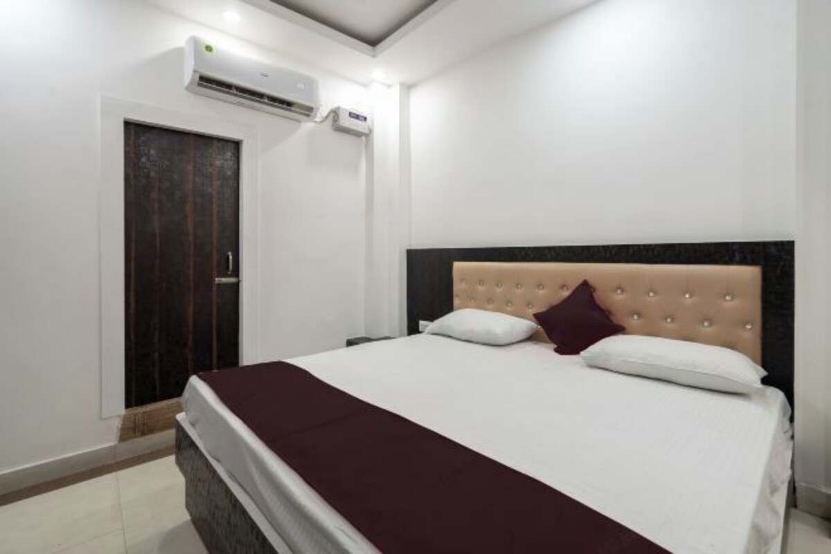 A hotel room with a bed, a dark door, and an air conditioning unit.