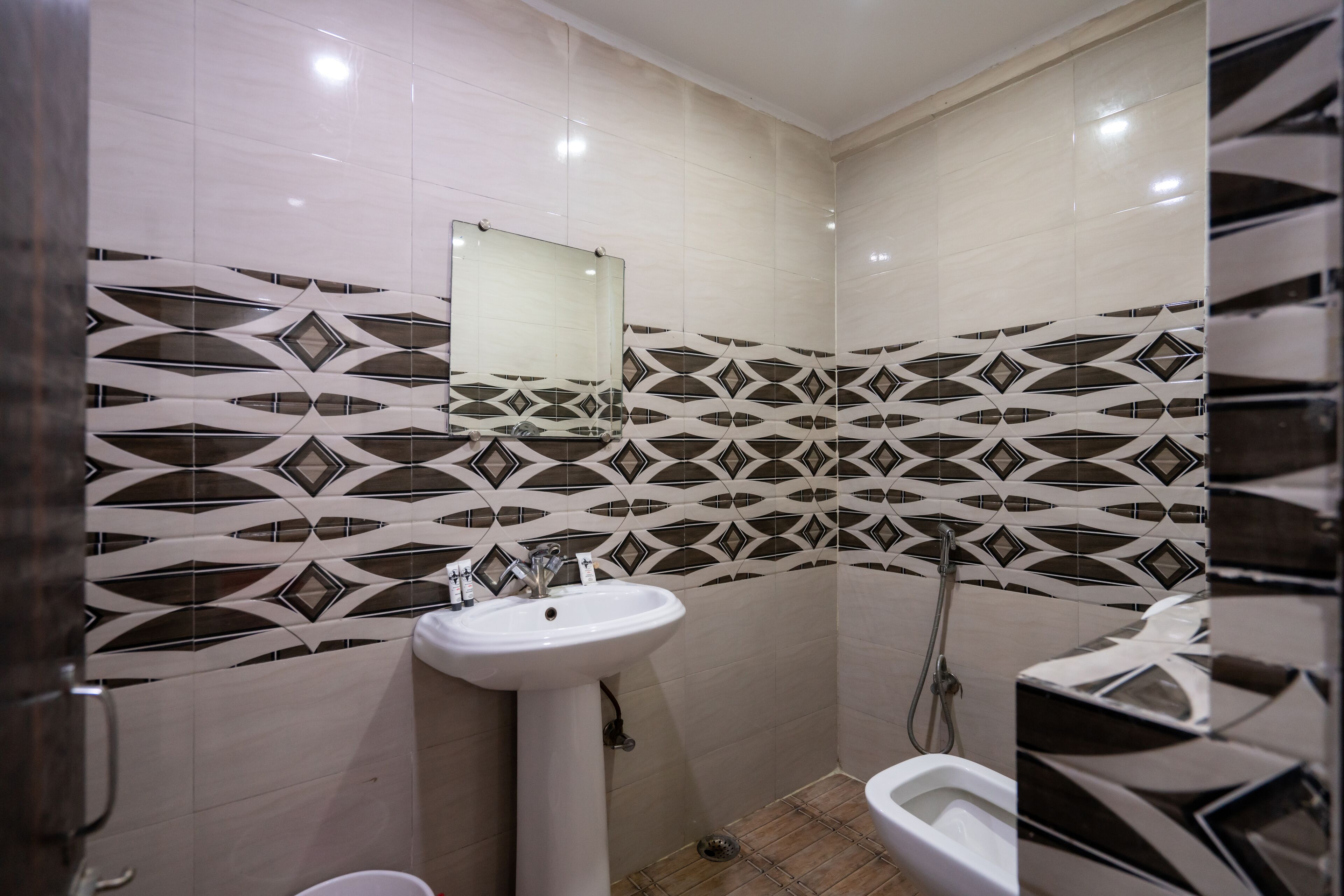 Un baño con lavamanos blanco, un espejo y ducha. Las paredes tienen un patrón geométrico de azulejos.