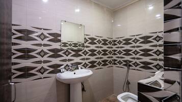 Un baño con lavamanos blanco, un espejo y ducha. Las paredes tienen un patrón geométrico de azulejos.