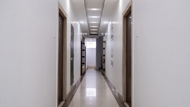 A long, narrow hallway with white walls and a shiny tiled floor. There are doors on both sides, and the ceiling has recessed lighting. - Nova Inn (Gorakhpur)