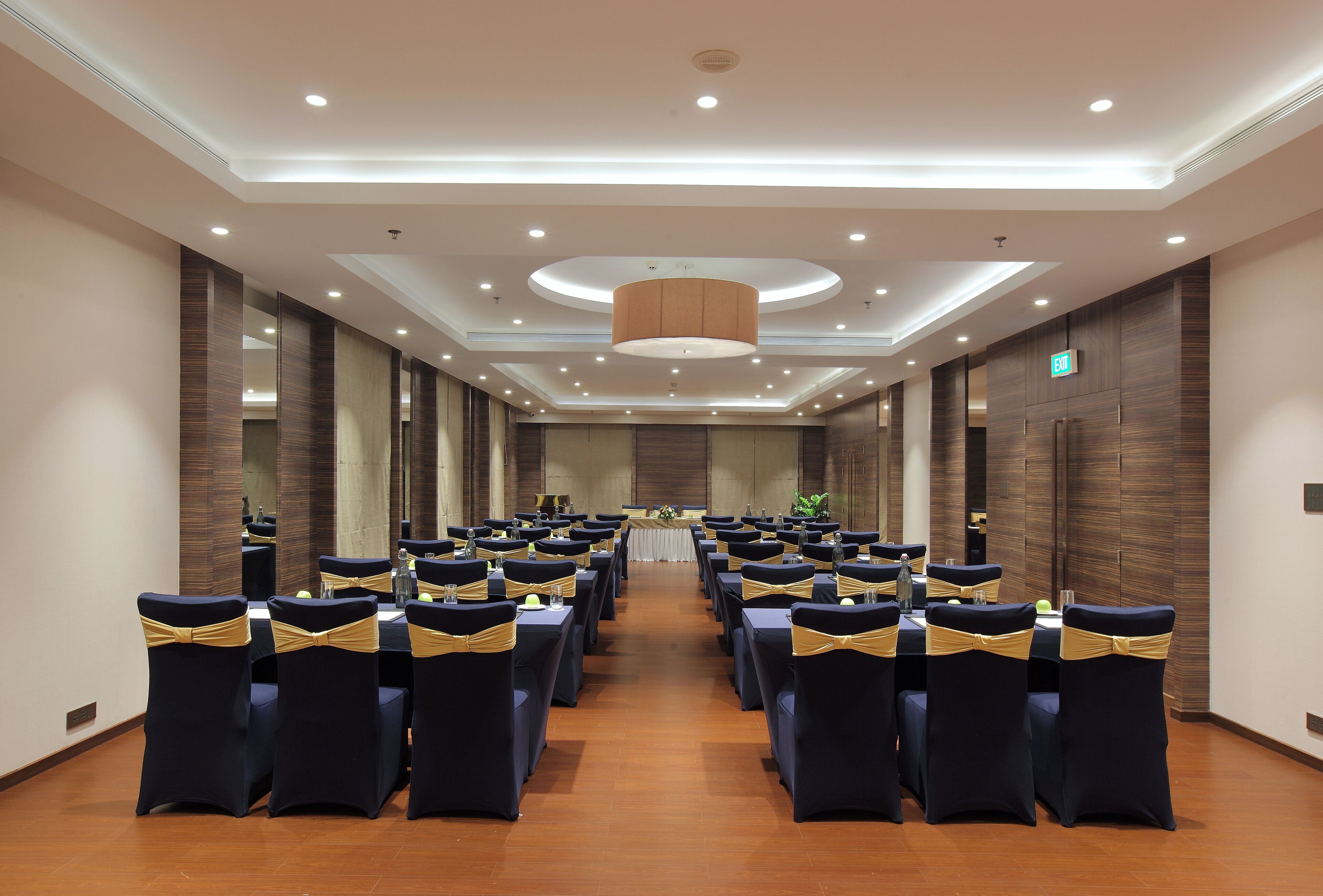 A conference room with rows of tables and chairs, a central stage, and a modern ceiling design.