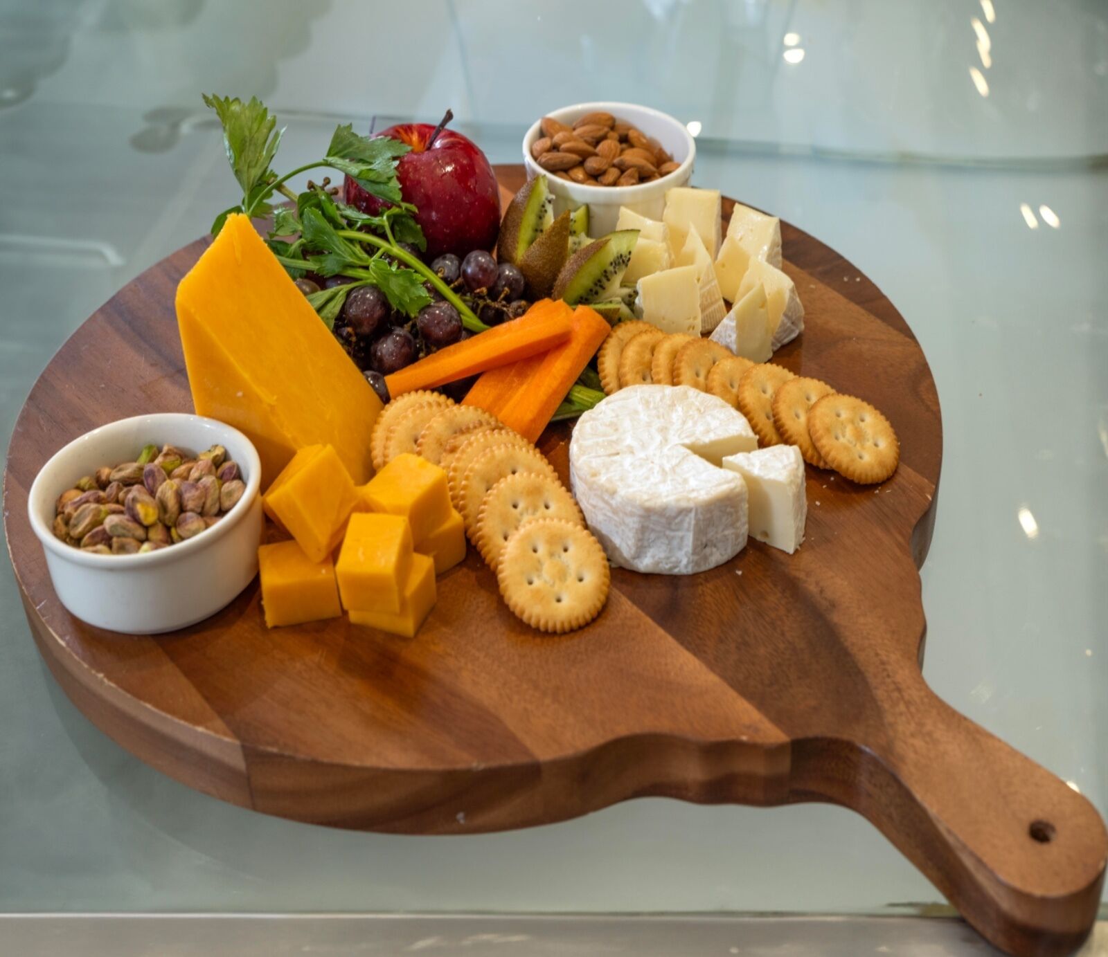 A wooden board with various cheeses, crackers, nuts, and fruits.