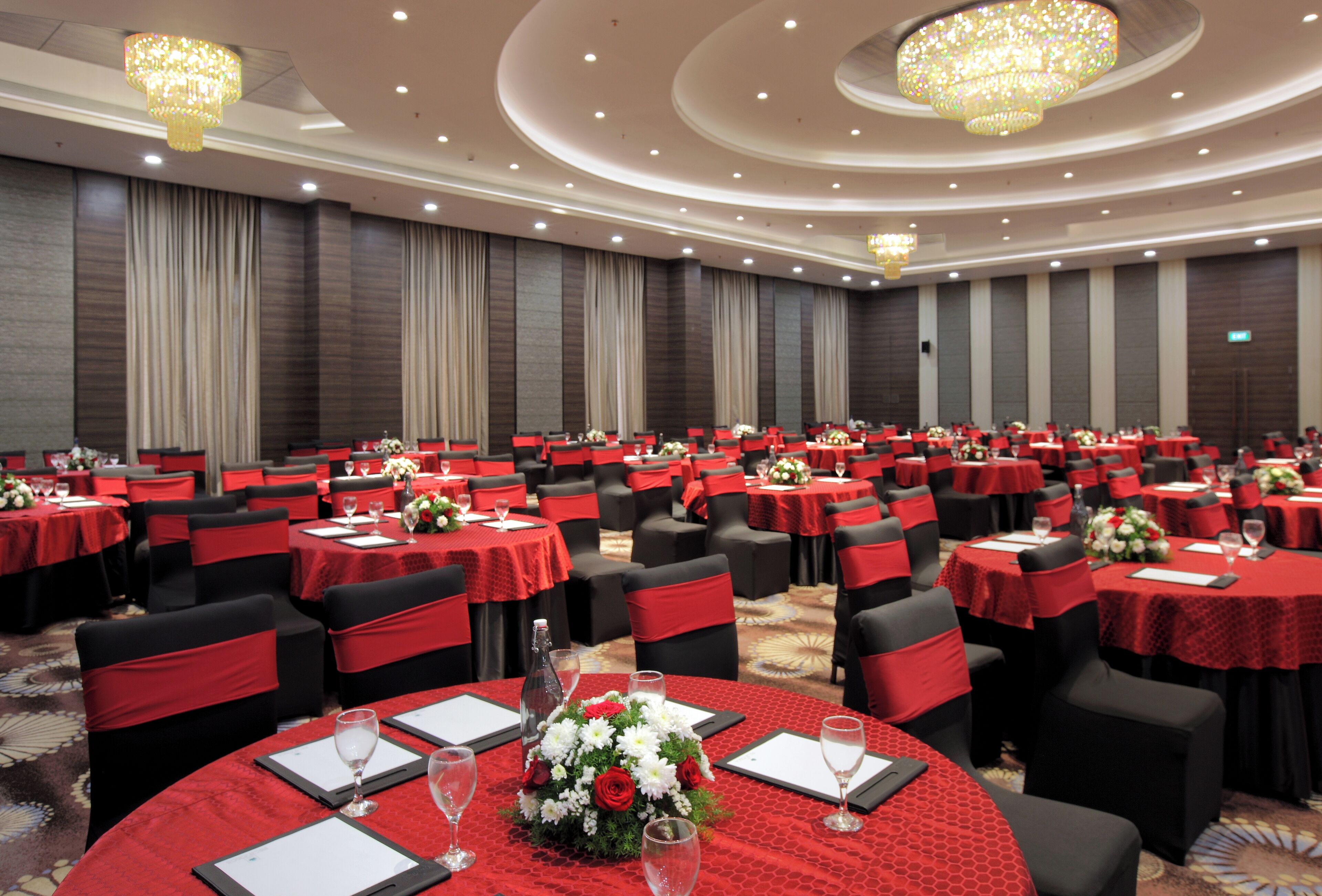 A banquet hall with round tables, black chairs, and red tablecloths.