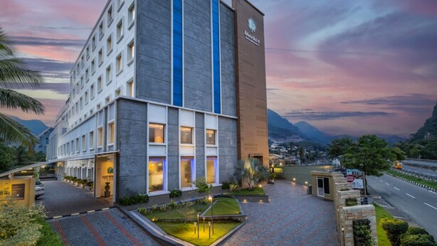 Un hotel moderno con una llamativa banda azul vertical, un jardín cuidado y vistas del paisaje circundante.