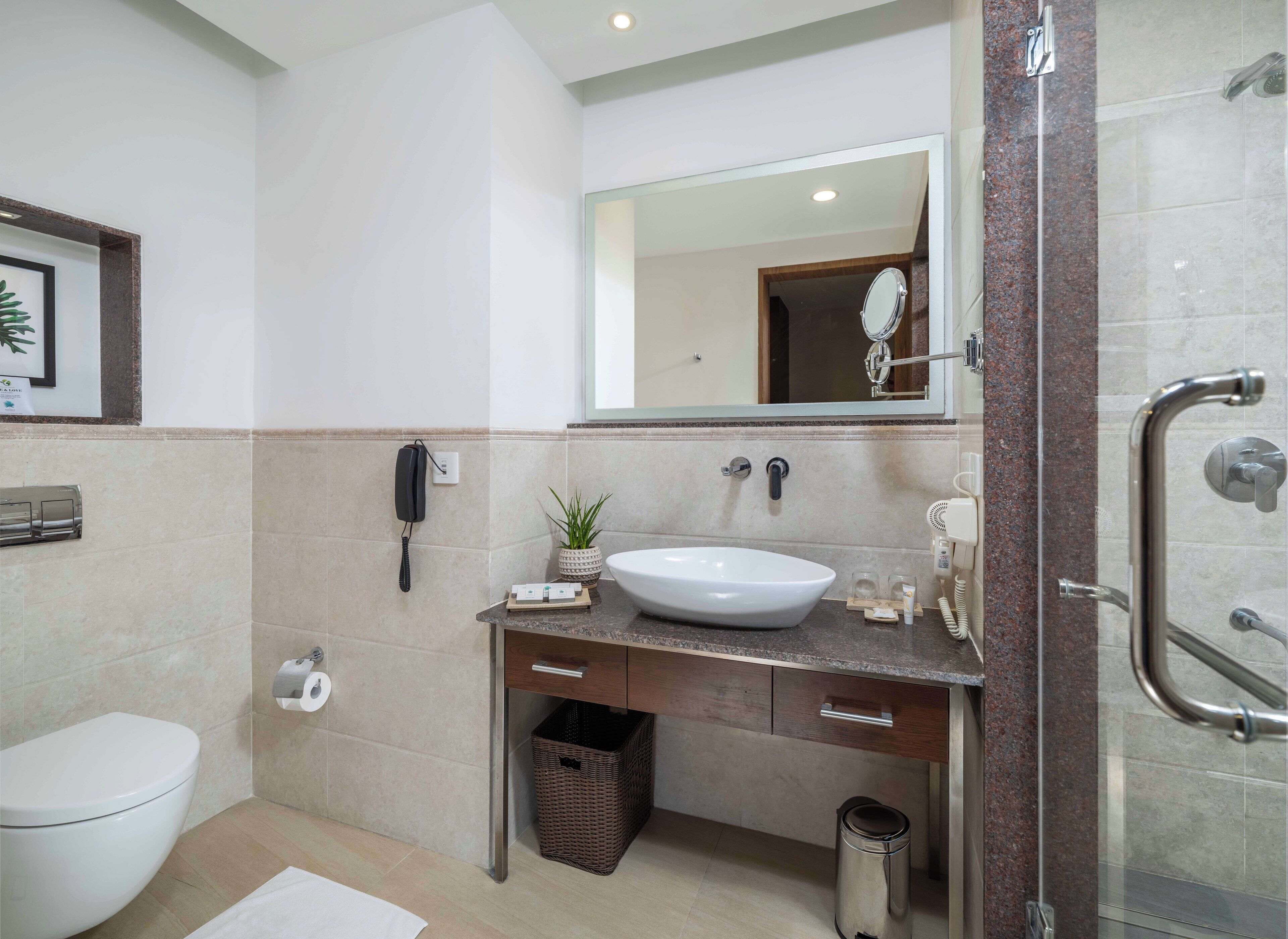 Un baño moderno con lavamanos blanco, espejo, teléfono y zona de ducha.
