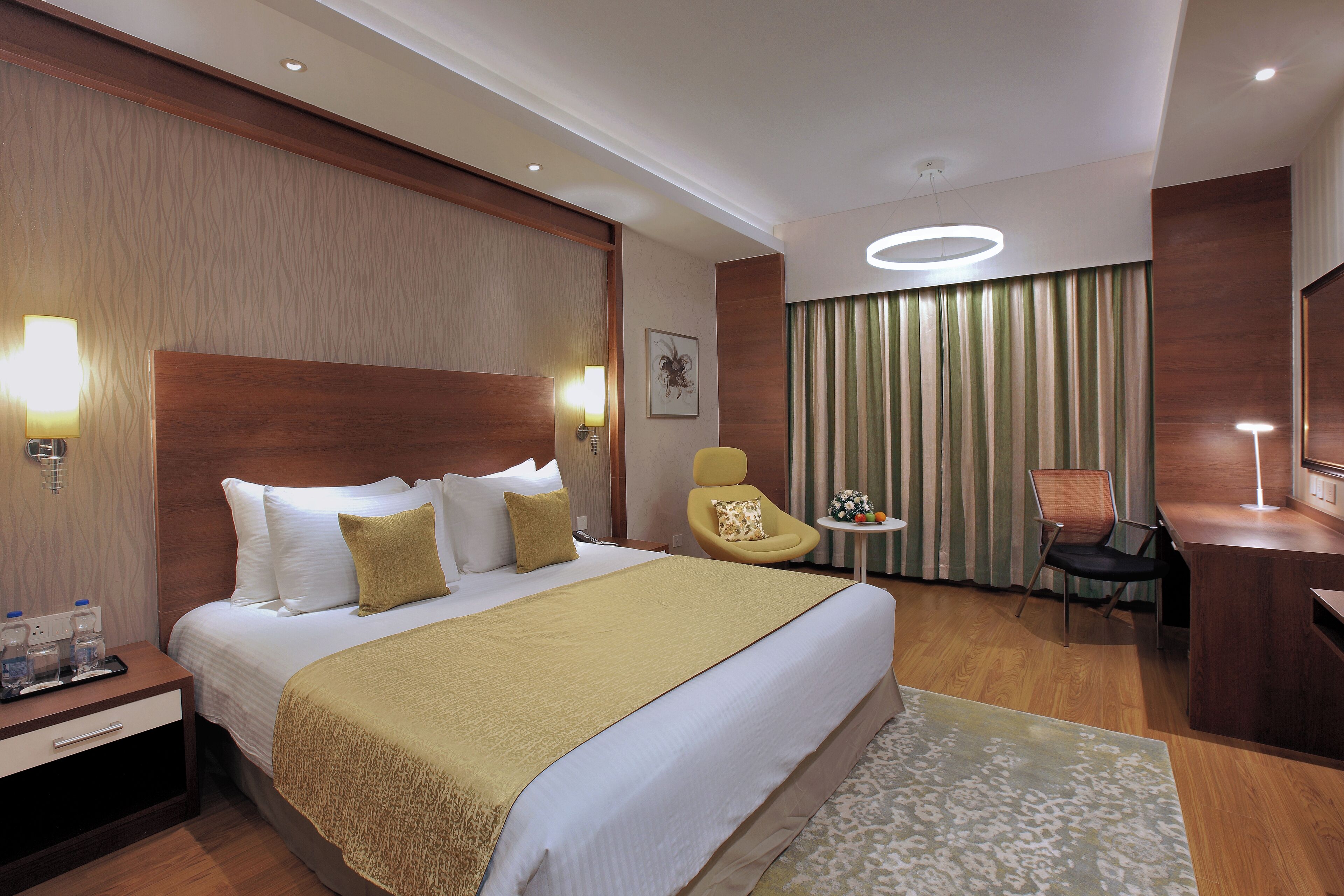 A hotel room with a large bed, bedside tables, a desk, a chair, and a small table with a lamp.