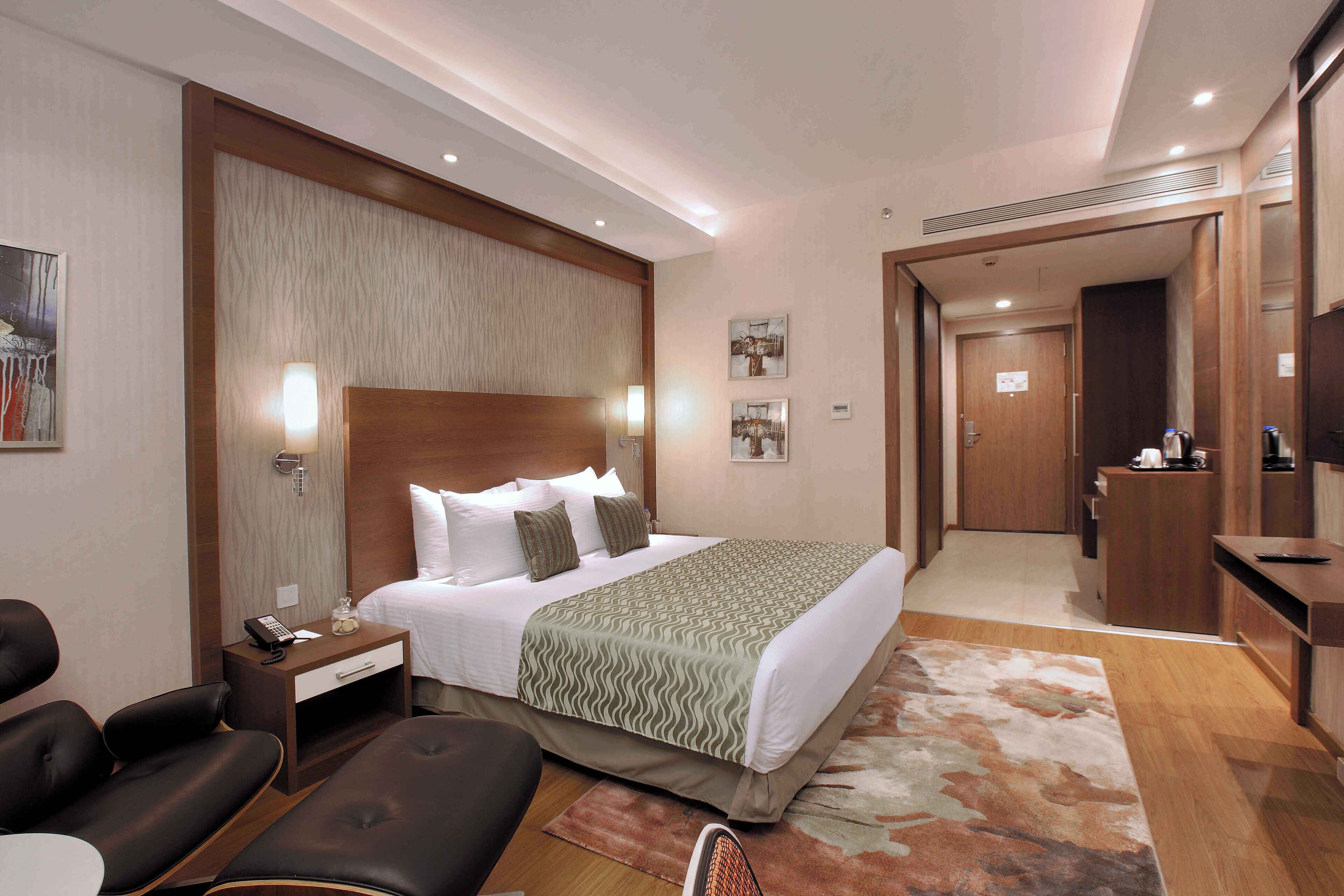 A hotel room with a large bed, a desk, a chair, and a bathroom visible through an open door.