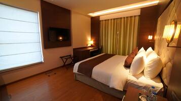 A hotel room with a large bed, a desk, a flat-screen TV, and a window with blinds.