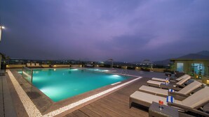 Una piscina en la azotea con agua cristalina, rodeada de sillones de descanso y una terraza de madera.