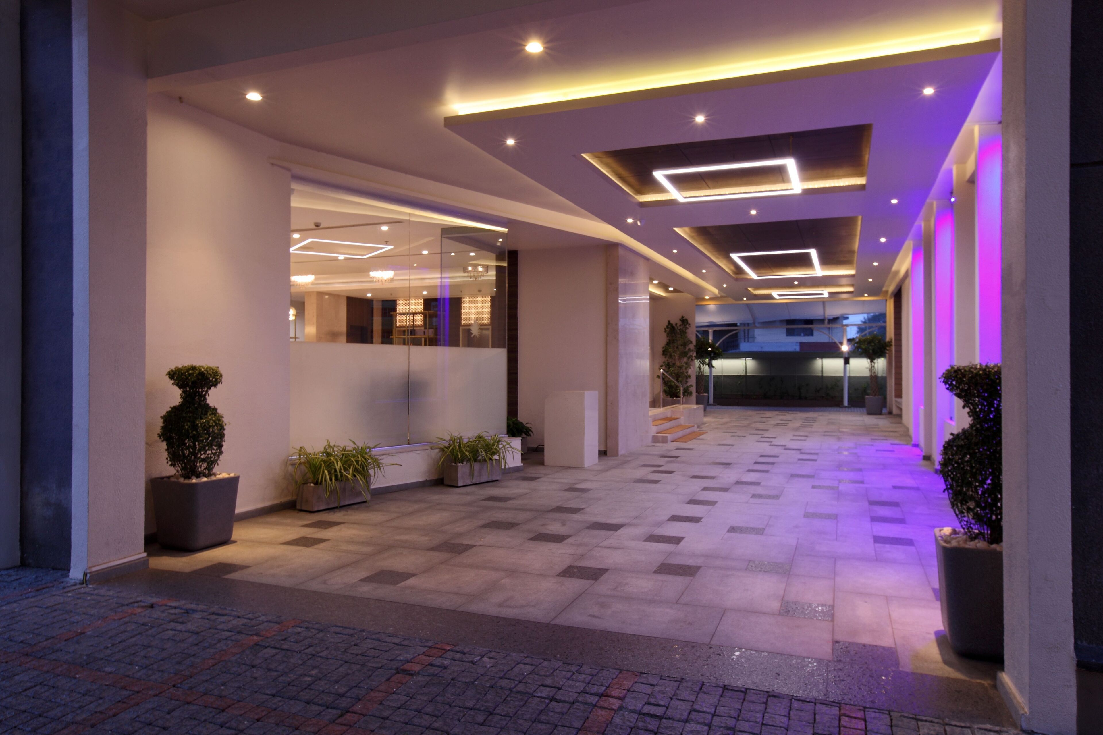 A modern hotel lobby with a checkered floor, potted plants, and recessed lighting.
