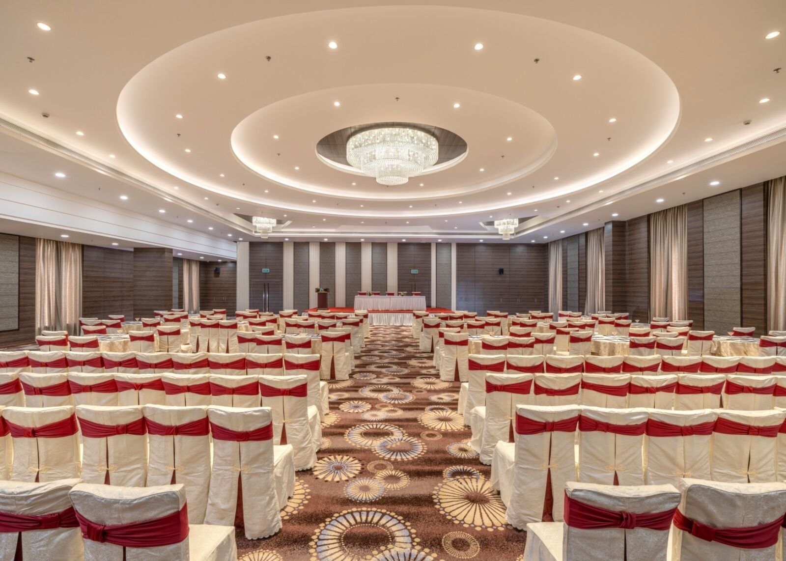 Une salle de conférence avec des rangées de chaises, une scène et un lustre.