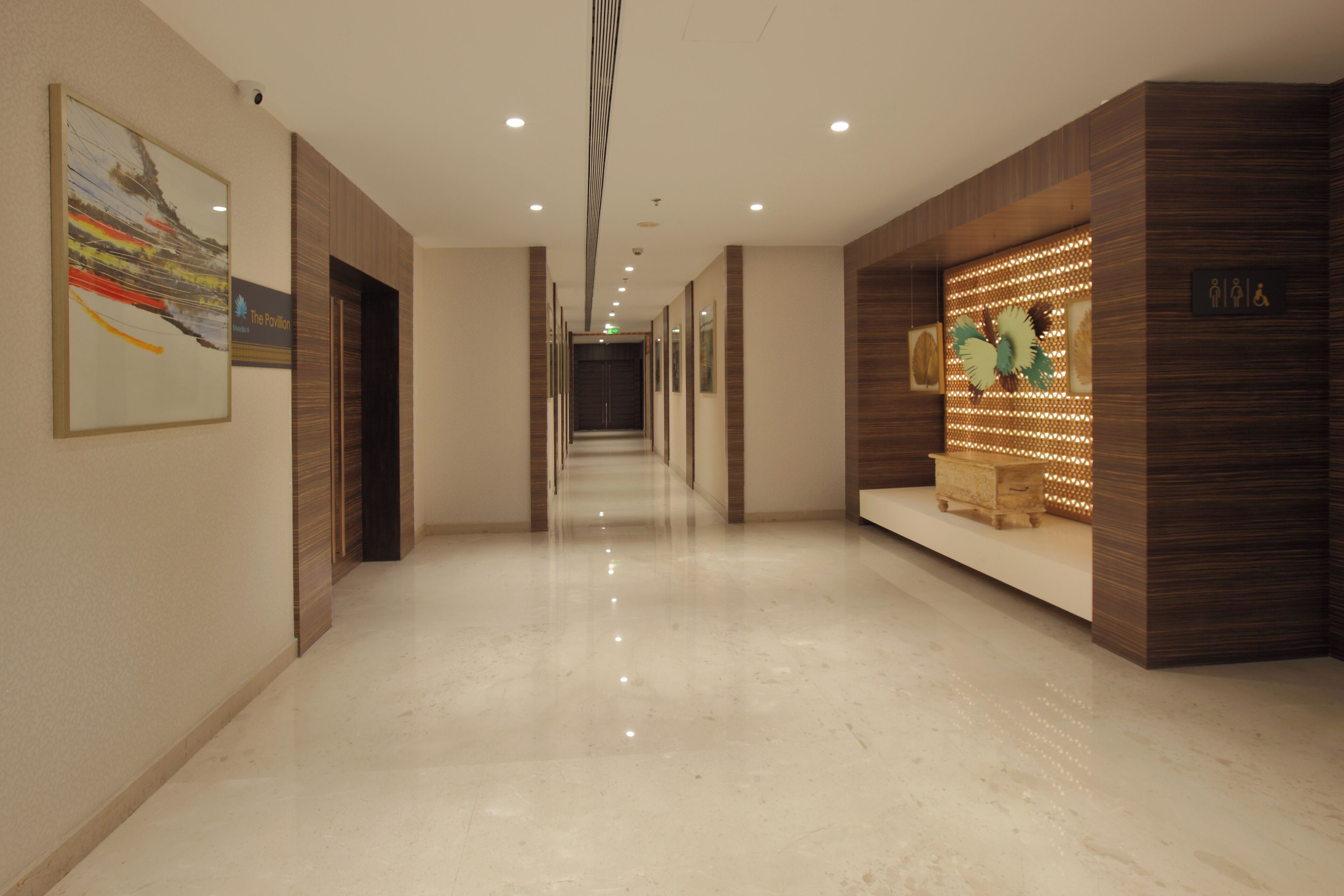 A hotel corridor with a polished marble floor, wooden paneling on the walls, and a reception area with a decorative display.