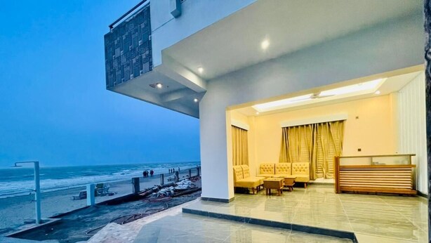 Eine moderne Hotelhalle mit Blick auf den Strand, eine Sitzecke mit gelben Stühlen und eine Rezeption.