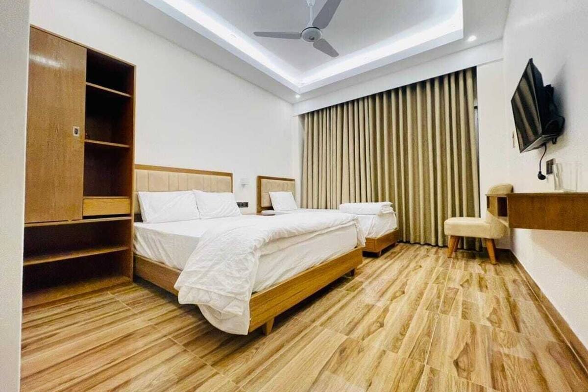 Ein Hotelzimmer mit zwei Betten, einem Deckenventilator, einem Fernseher und Holzboden.