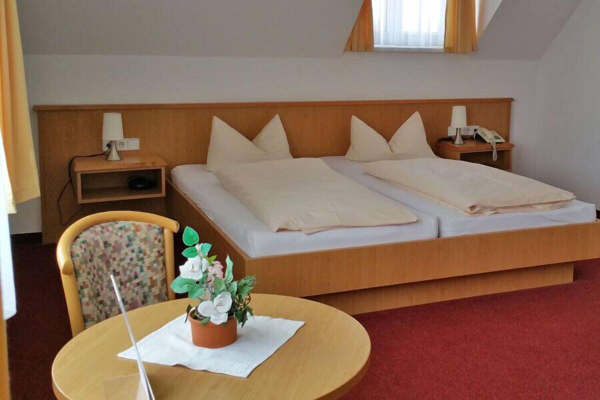 Ein Schlafzimmer mit Bett, Nachttischen, einem Sessel, einem Tisch mit Pflanze und einem Fenster.