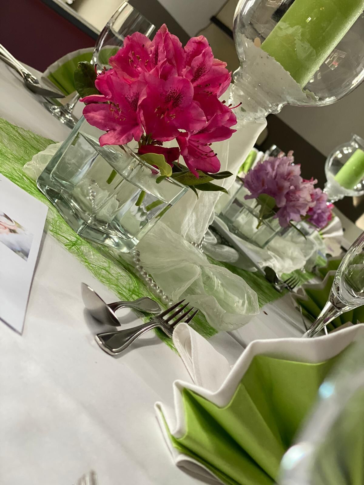 A table set with clear glassware, pink and purple flowers, and green napkins.