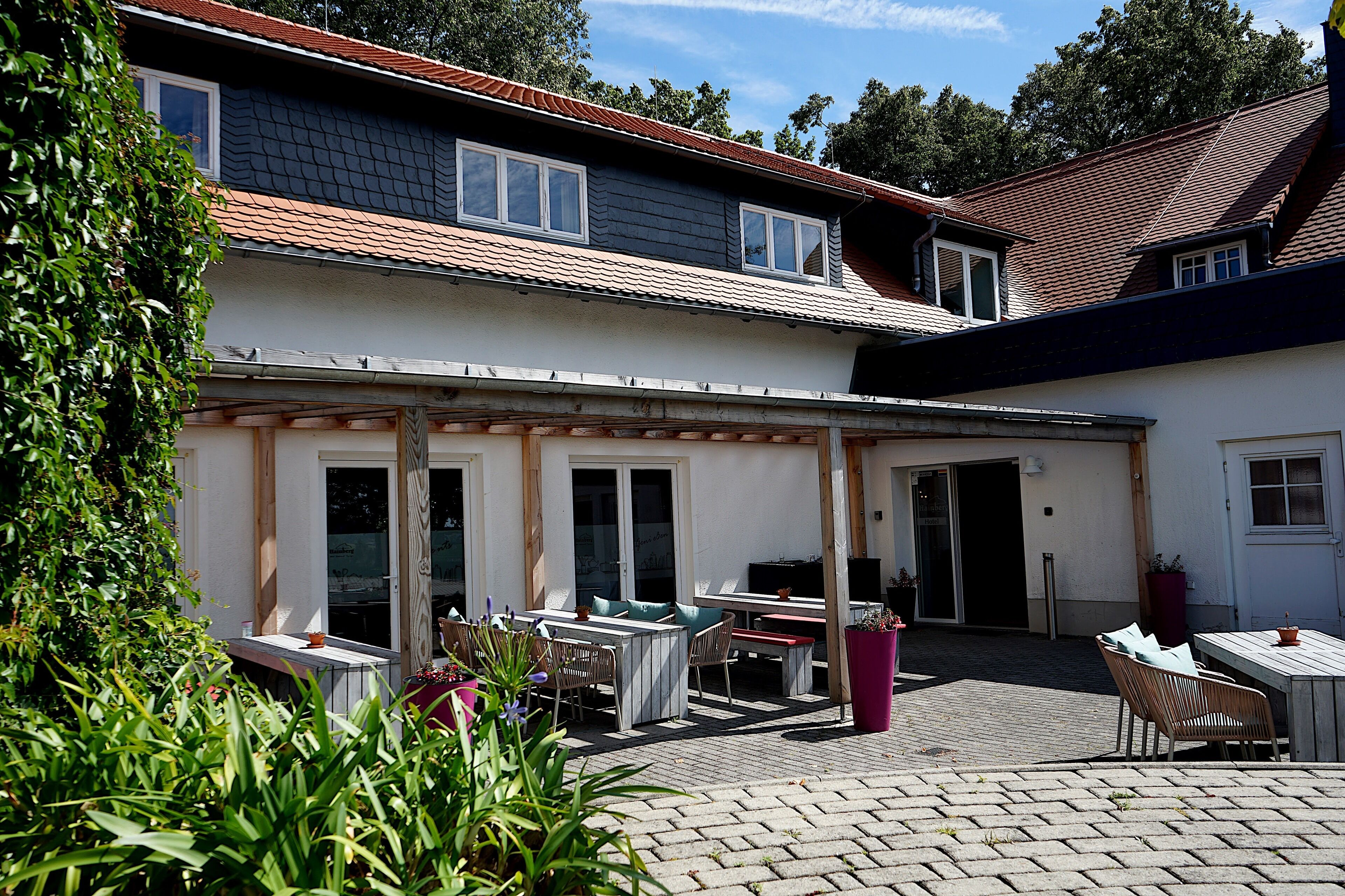 Eine überdachte Terrasse mit Essbereich, Grill und kleinem Garten.