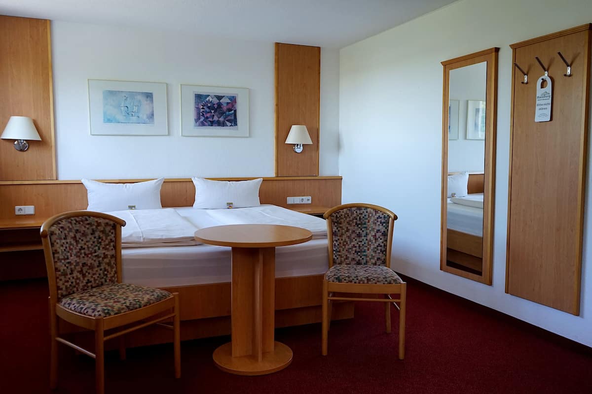 Ein Hotelzimmer mit einem Bett, zwei Stühlen, einem kleinen runden Tisch und einem Spiegel.
