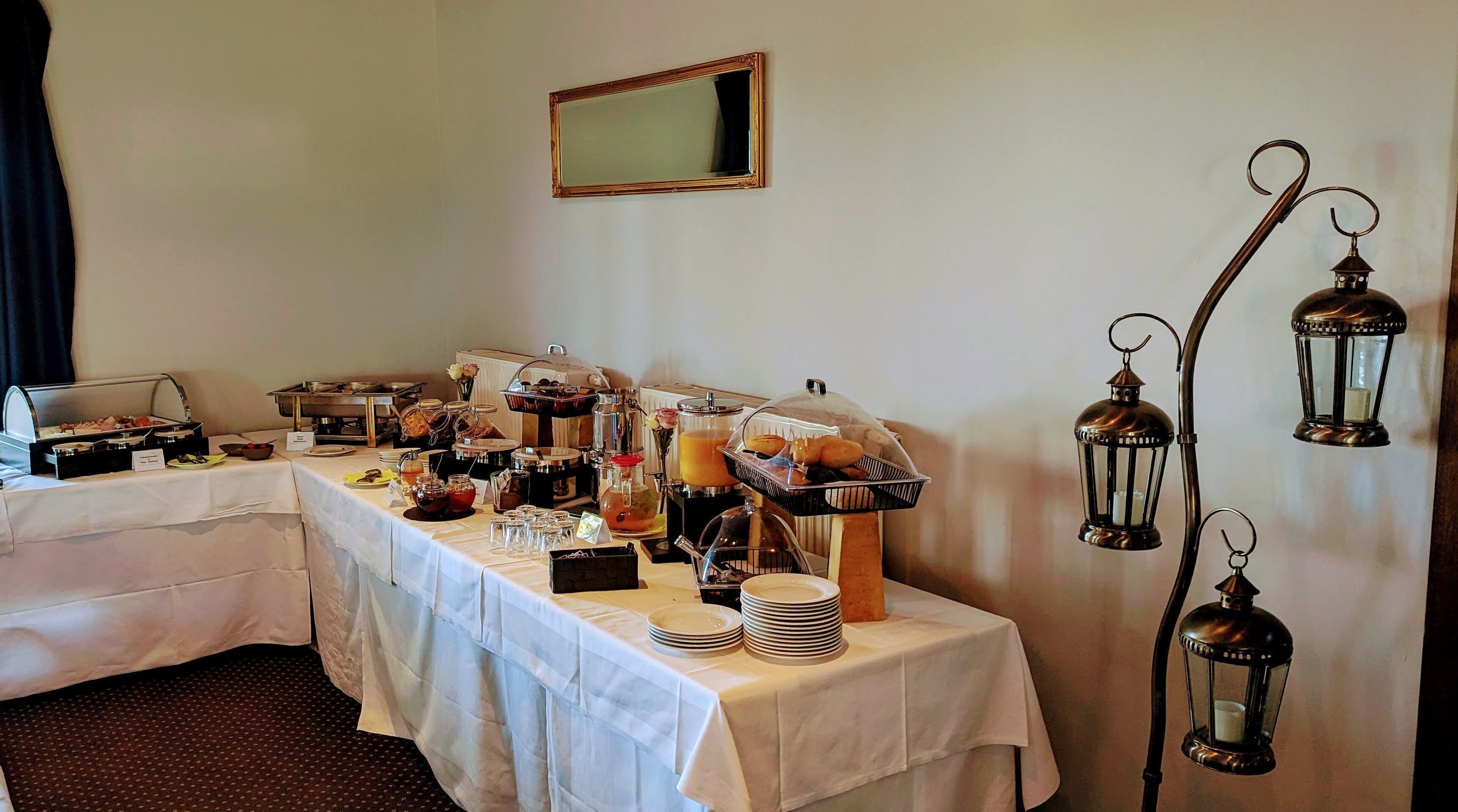 A buffet setup with various food items and a coffee station, a mirror on the wall, and decorative lanterns.