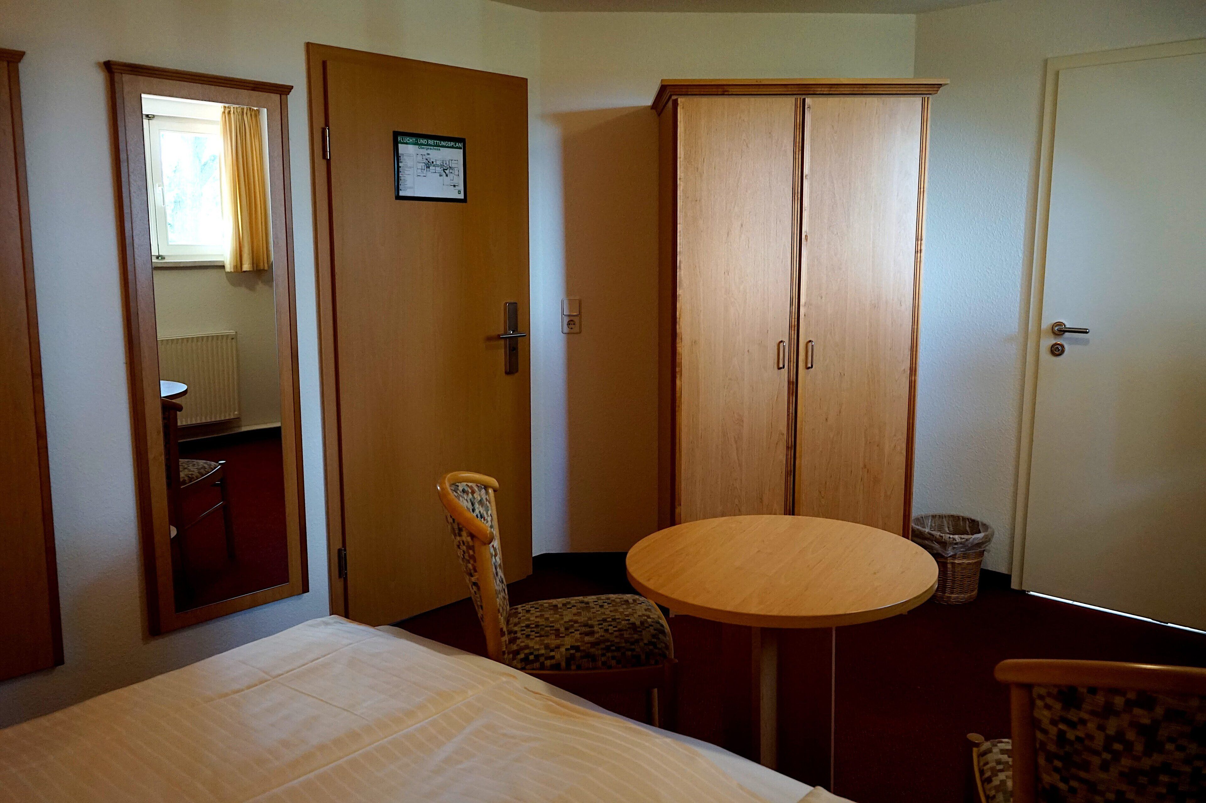 Una habitación de hotel con cama, una mesita redonda, una silla, un armario y un espejo.