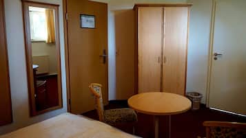 Una habitación de hotel con cama, una mesita redonda, una silla, un armario y un espejo.