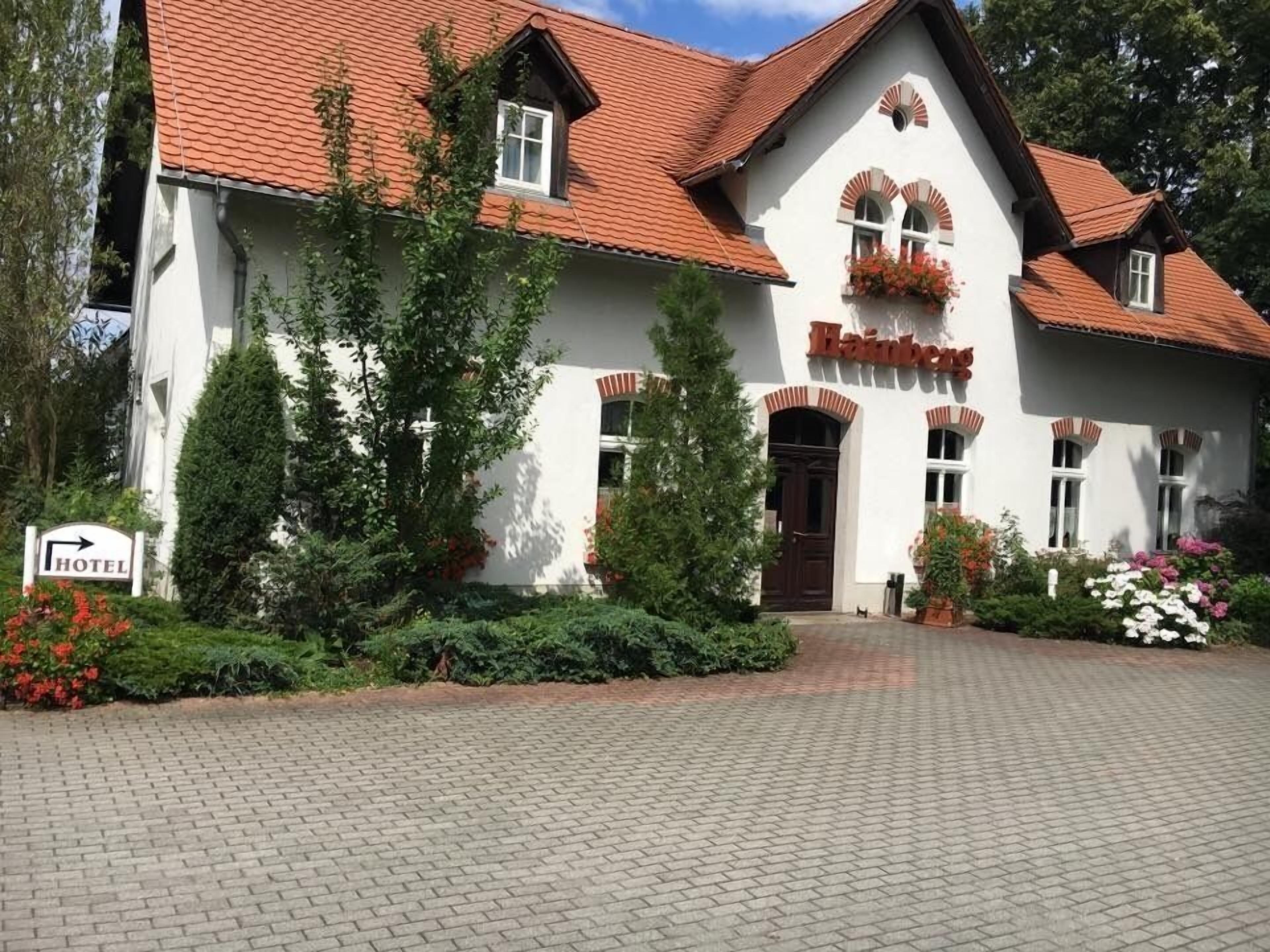 A traditional white building with a red-tiled roof, a sign indicating a hotel, and a well-maintained garden with various plants and flowers.