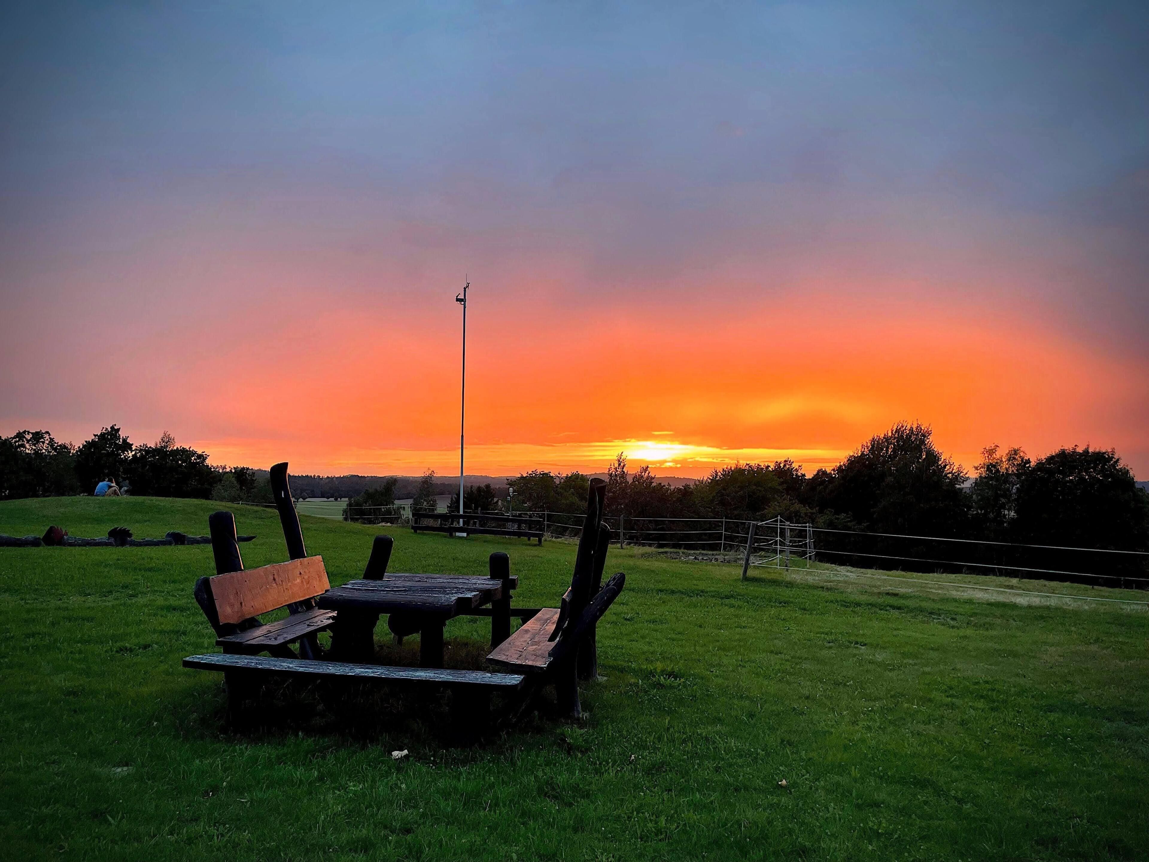 Una mesa de picnic y bancos en un campo cubierto de hierba, con un atardecer de fondo.