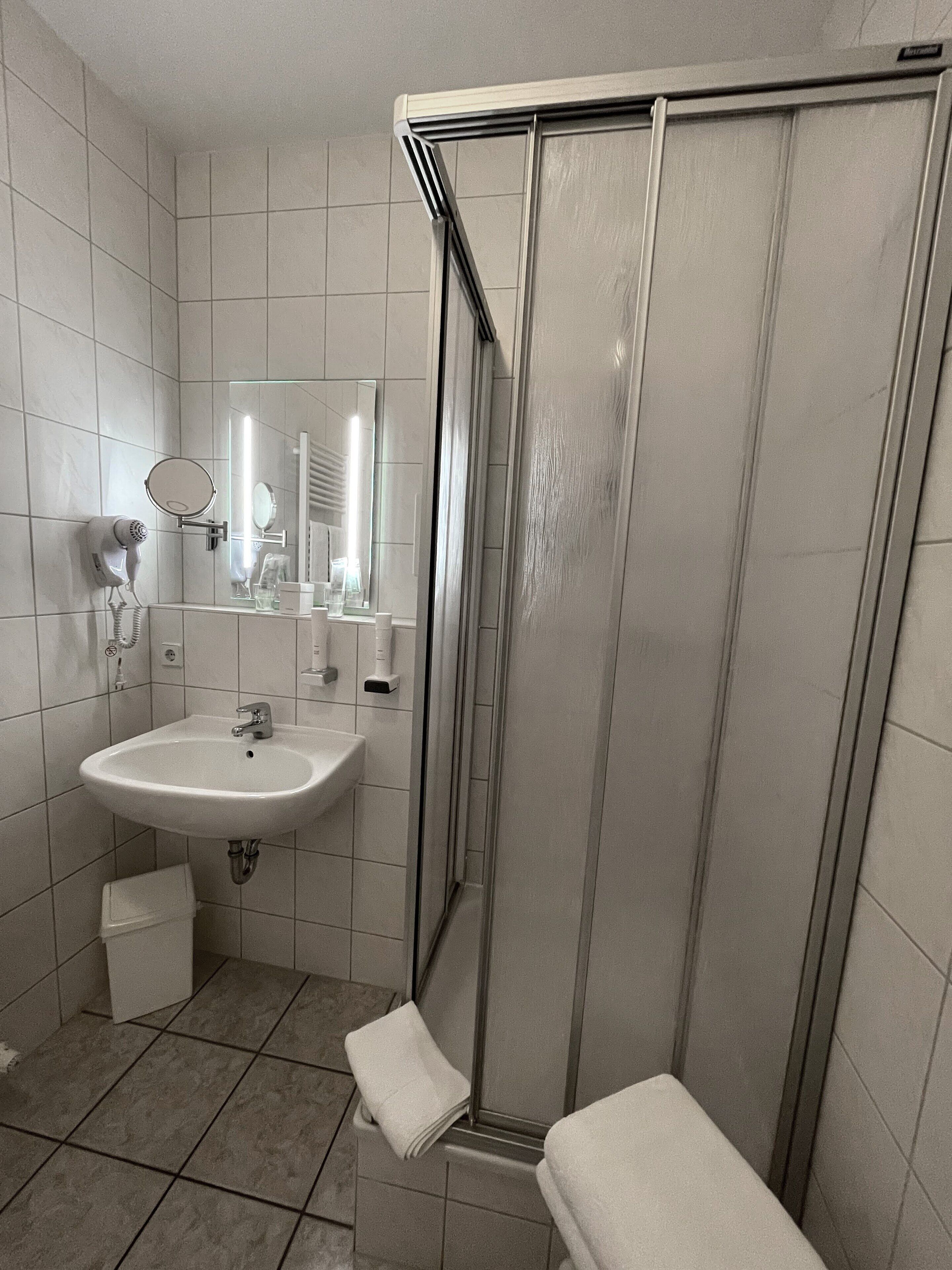 Casa de banho com uma pia branca, espelho, secador de cabelo e cabine de duche em vidro.