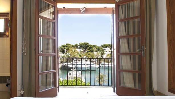 An open door leading to a balcony with a view of a marina and boats.