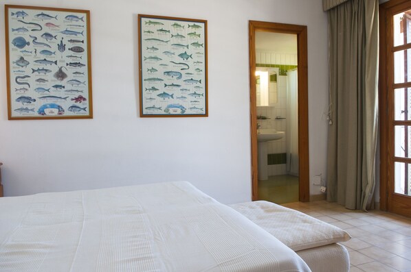Un dormitorio con una cama, dos ilustraciones enmarcadas de peces en la pared y un baño visible a través de una puerta abierta.