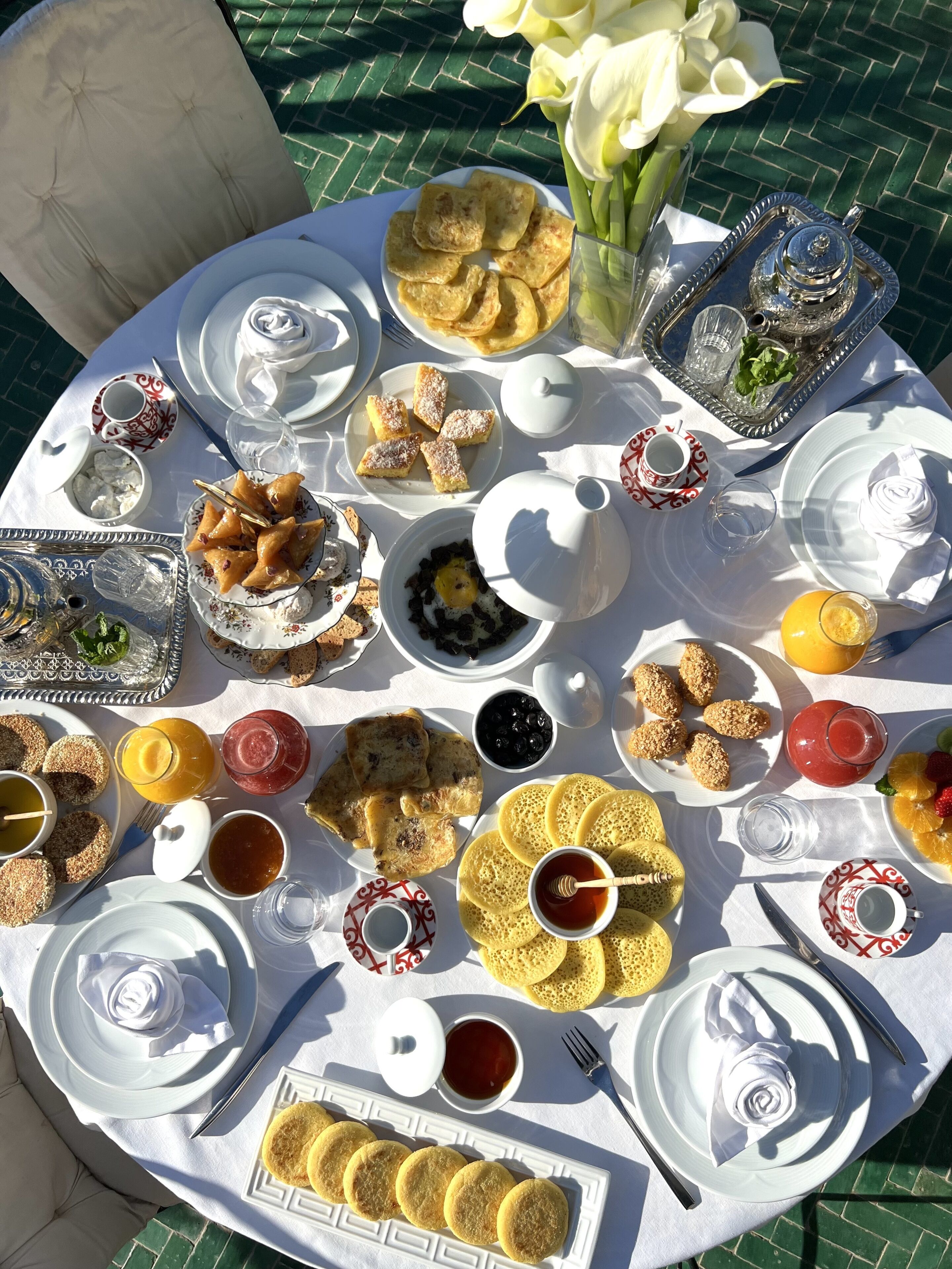 A round table set with a variety of breakfast items including pastries, fruits, and beverages, arranged on a white tablecloth.